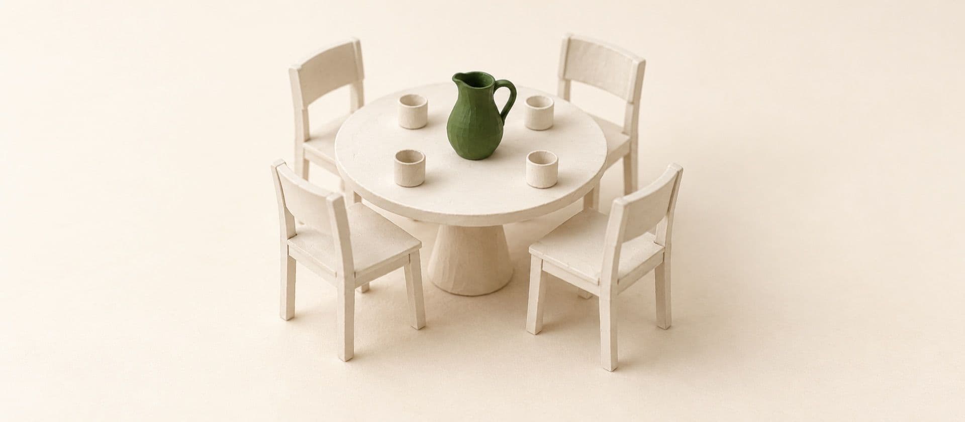 A cream study model of a small round table with four chairs pulled up to it, a pitcher and four cups on the table, with the pitcher in green.
