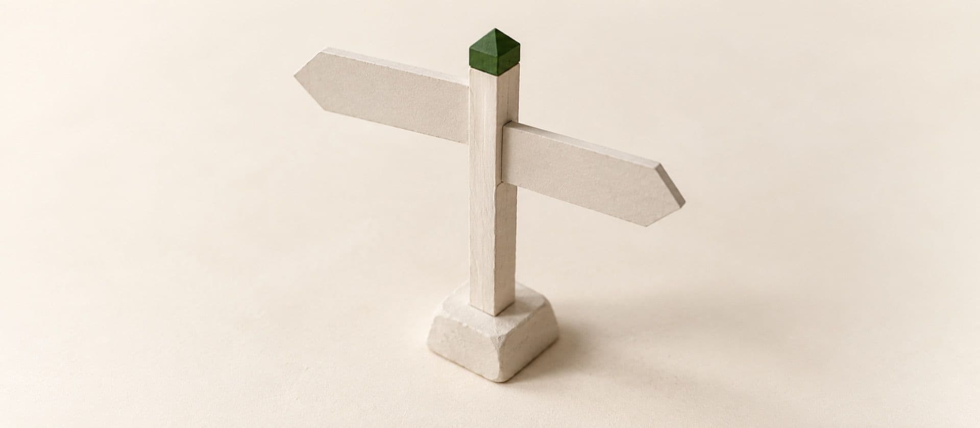 A cream study model of a wooden signpost with two blank arms pointing in different directions, with the cap on top of the post in green.