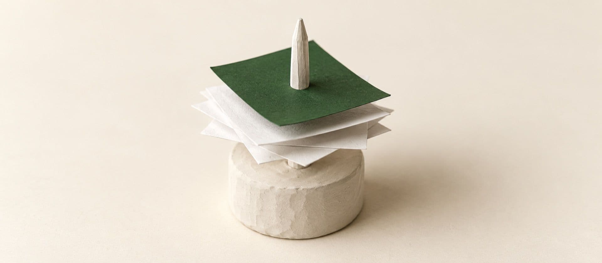 A cream study model of a desk receipt spike with a few blank paper slips pushed onto it, with the top slip in green.