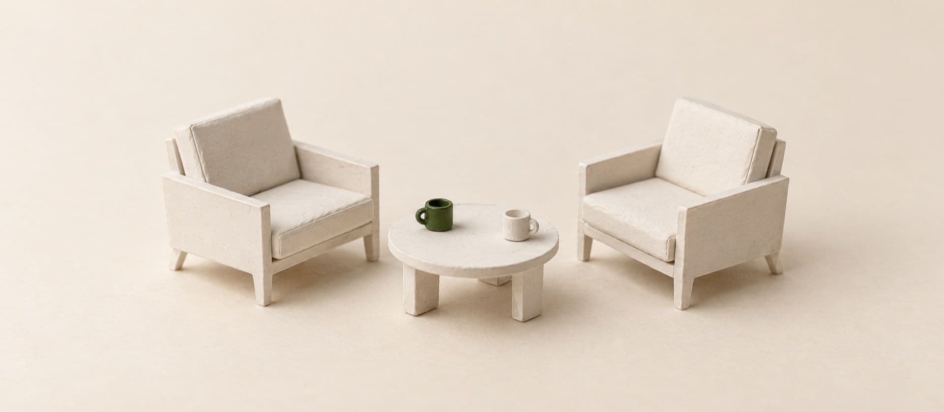 A cream study model of two armchairs facing each other across a small low table with two cups, with one of the cups in green.