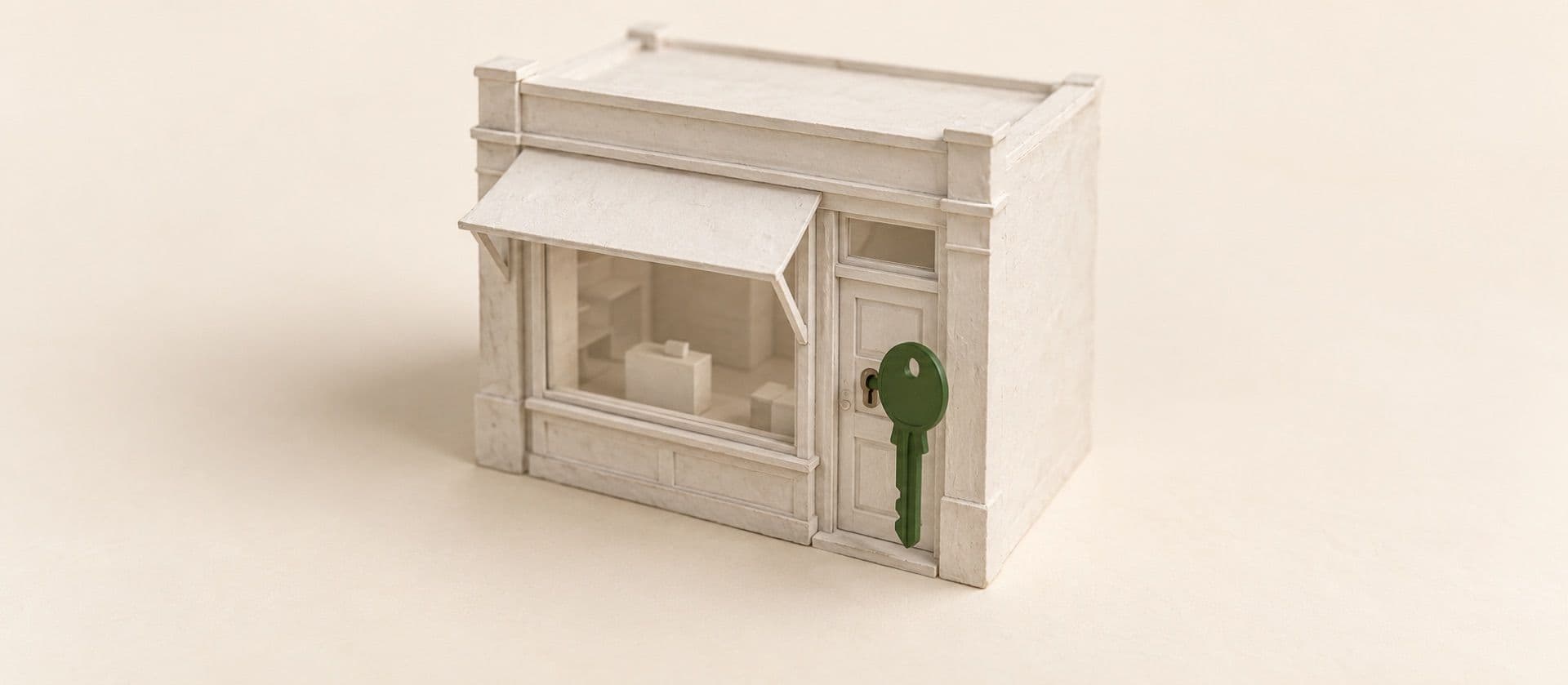 A cream study model of a small model of a storefront with a large key standing in its door lock, with the key in green.