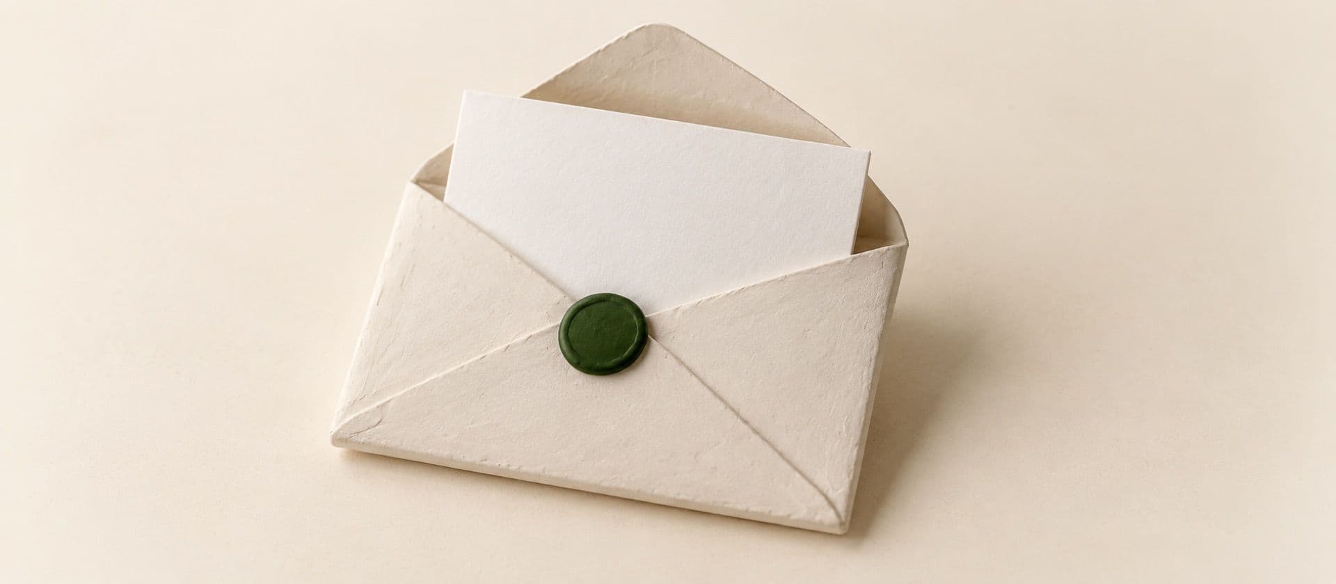 A cream study model of an envelope with a folded blank letter drawn halfway out of it, with a round seal on the envelope flap in green.