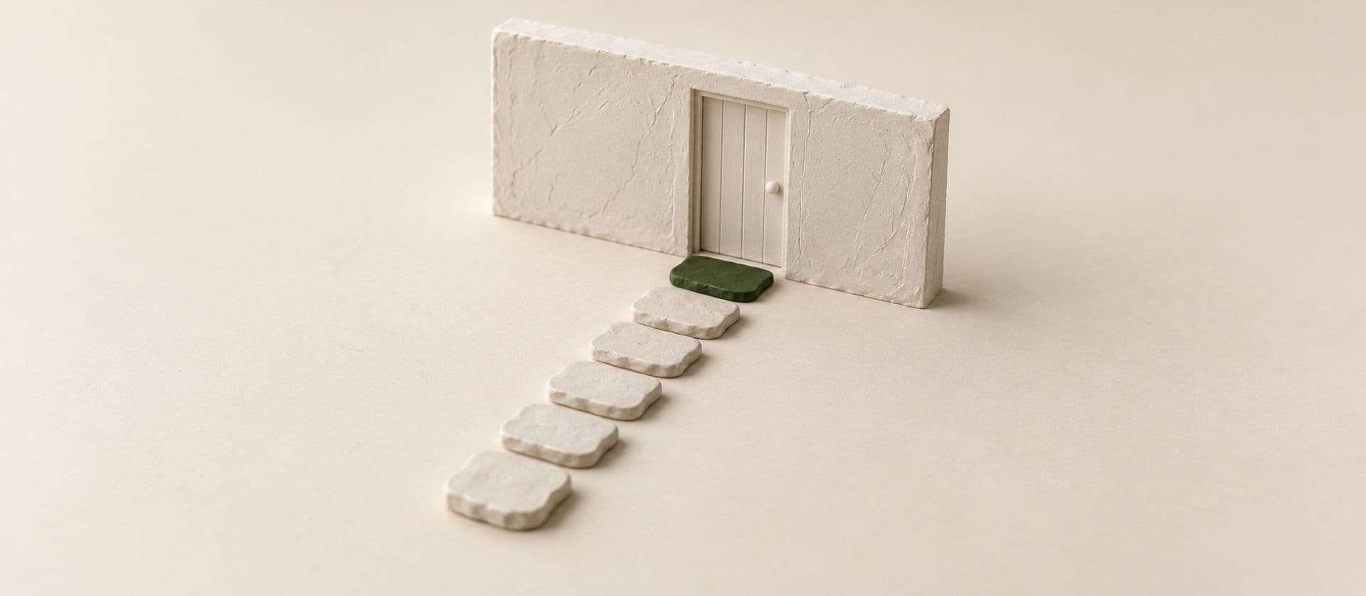 A cream study model of a line of seven flat stepping stones leading to a small door in a short piece of wall, with the last stepping stone in green.