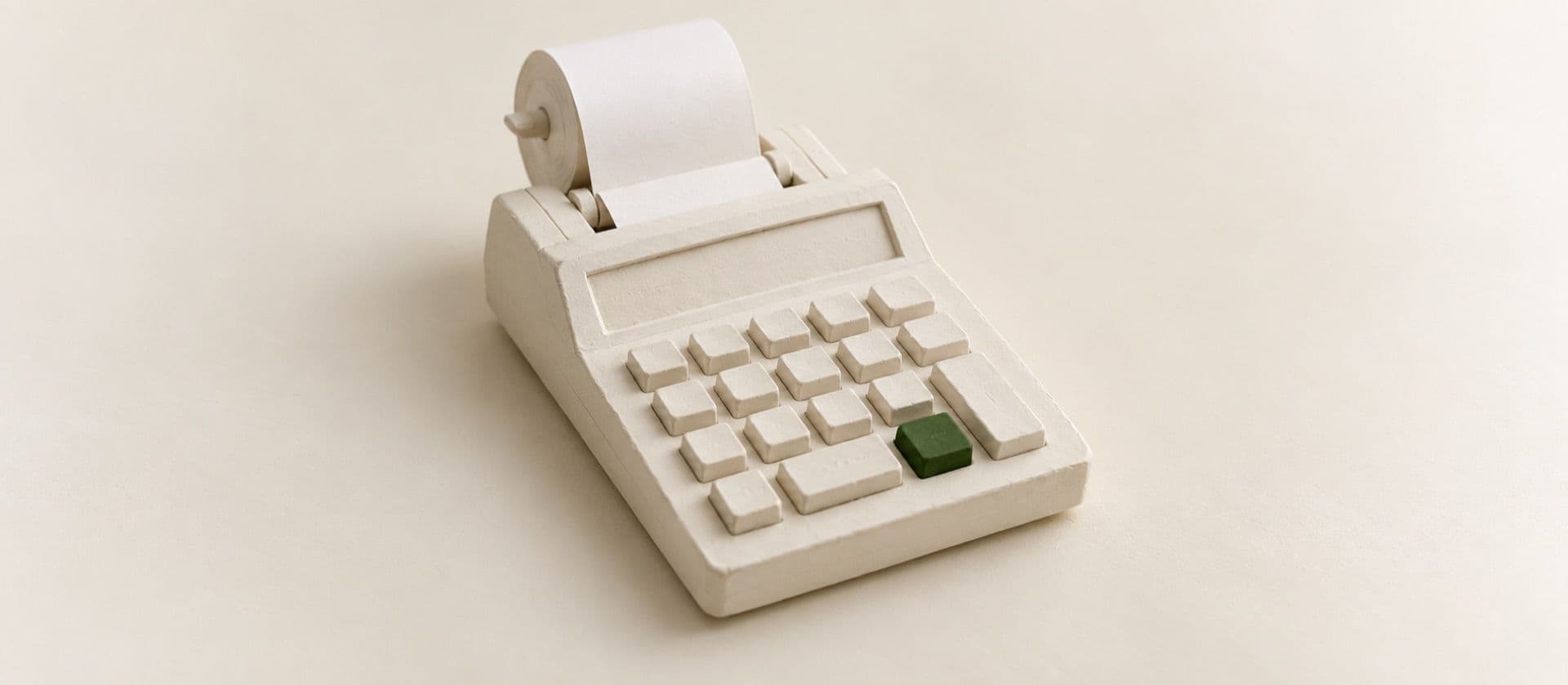 A cream study model of a chunky desk calculator with blank raised keys and a blank paper roll curling out of the top, with one key in green.