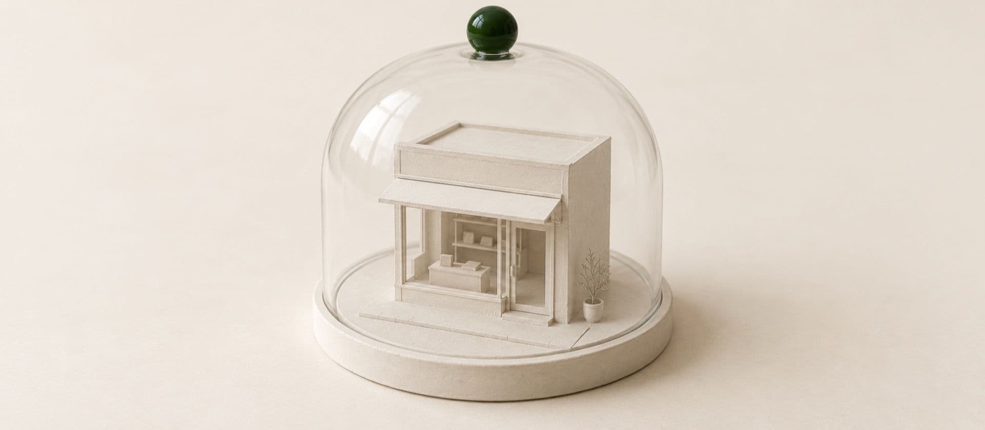 A cream study model of a small shop model under a glass display dome on a round base, with the knob on top of the dome in green.